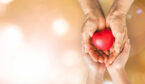 A young and old pair of hands hold a heart together