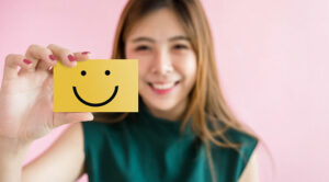 Happy person holds up a post it note with a smiley face on it