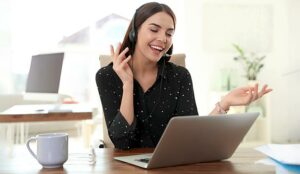 A woman with a headset on, talks animatedly in front of a laptop