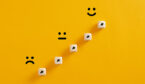 Arrows on wooden cubes pointing from a sad expression towards a happy one.