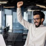 Person sitting in office in front of laptop and rejoicing in success