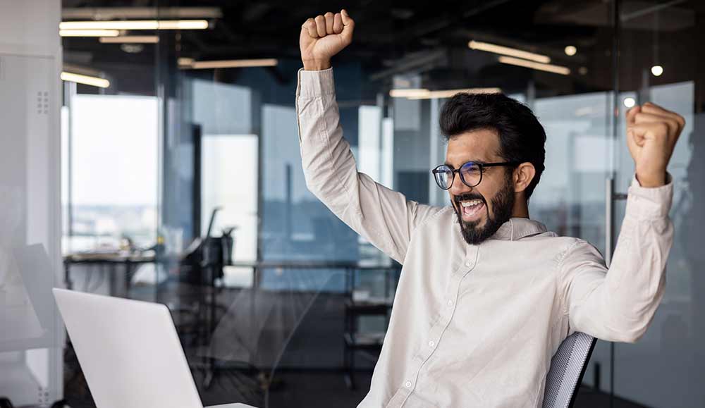 Person sitting in office in front of laptop and rejoicing in success