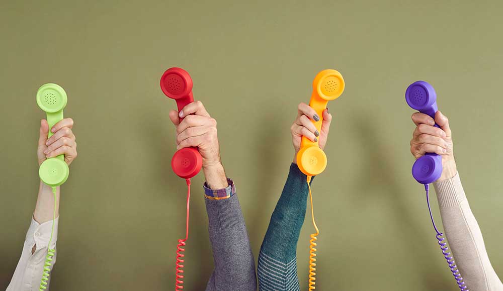 Group of people holding different colourful landline phones