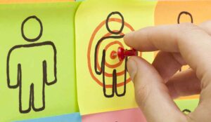 Hand pinning a sticky note in the center of a customer target on cork board