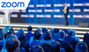 Audience attentively listening to keynote speaker at a corporate event with blurred conference background.