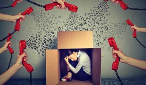 Stressed young business woman sitting hiding in a box overwhelmed by too many red telephone calls